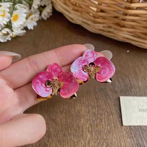 Detaillierte Nahaufnahme von rosa Emaille-Orchideenblüten-Ohrringen mit Goldakzenten