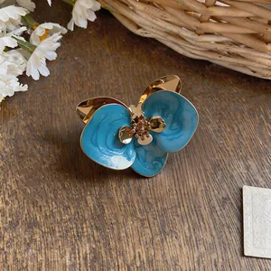 Detail eines blauen Emaille-Blumenohrrings mit Goldakzenten auf rustikalem Holzgrund.