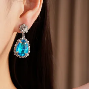 Close-up view of a blue water droplet earring with sparkling crystals on a model's ear.