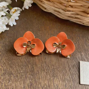 Detailaufnahme von orangefarbenen Emaille-Blumenohrringen mit eleganten goldfarbenen Akzenten