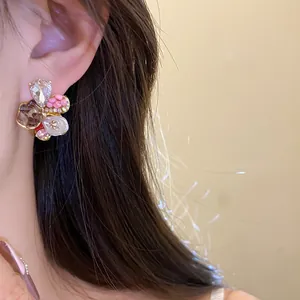 Close-up of elegant floral earrings with sparkling rhinestones and pink beads on model ear.