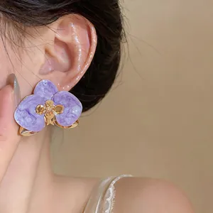 Nahaufnahme eleganter lila Orchideen-Ohrstecker mit Tropföl-Effekt am Ohr getragen
