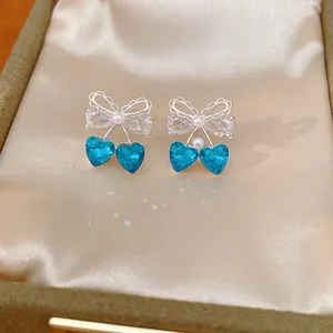 Close-up of bow earrings with blue heart crystals and pearl accents in a jewelry box