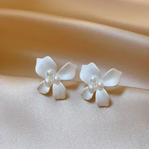 Close-up of elegant white flower earrings with pearls on champagne satin background.