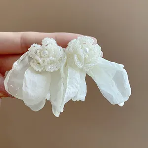 Close-up of elegant chiffon flower stud earrings with pearl and bead detail.