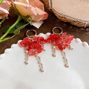 Elegantes pendientes de borla de flores rosas con perlas artificiales en plato de porcelana.
