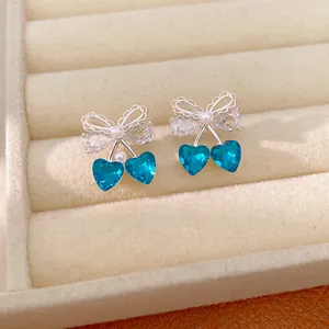 Detail view of bow earrings with blue heart-shaped stones and delicate pearl accents