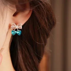 Detailed macro view of elegant cherry bow stud earrings with blue heart crystals on a model
