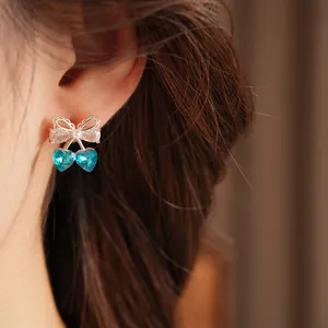 Close-up view of elegant bow cherry earrings with blue heart-shaped crystals and pearl