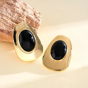 Vintage gold metal geometric stud earrings with black oval resin centers on textured stone