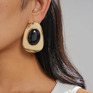 Detailed close-up of oversized retro gold metal earrings with black oval resin inlay
