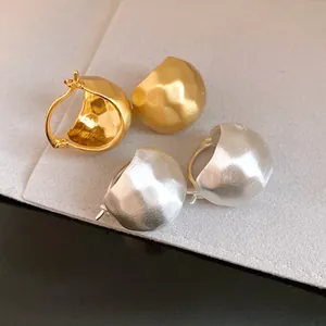 Close-up of matte brushed semi-circular dome hoop earrings in gold and silver finish