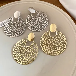 Elegante kreisförmige, hohl geschnittene Ohrhänger in Gold und Silber auf einem Teller