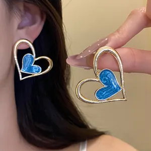 Elegantes pendientes de corazón en esmalte azul con marco dorado en la oreja y la mano