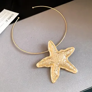 Close-up detail of a large gold-toned starfish pendant on a thin metal choker necklace.