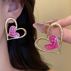 Detalle de pendientes en forma de corazón rosa y dorado en la oreja y la mano