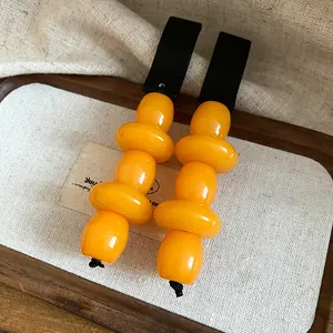 Detail view of retro resin earrings with yellow beads and black wood top on a tray.