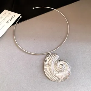Close-up of a silver nautilus shell pendant necklace on a gray textured surface
