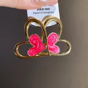 Primer plano de pendientes de corazón dorados con esmalte rosa y etiqueta de precio.