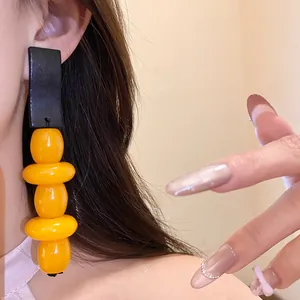 Detailed close-up of vintage yellow resin drop earrings with black geometric accents