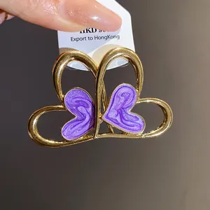Detalle macro de pendientes de corazón dorados con acabado de esmalte veteado púrpura