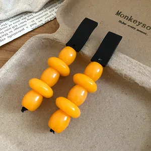 Close-up of retro earrings featuring black wood tops and vibrant orange resin beads