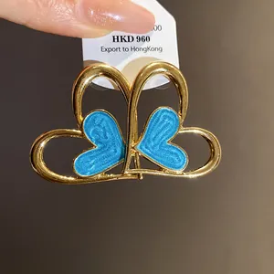 Vista detallada de pendientes de corazón vintage con esmalte azul y marco dorado.