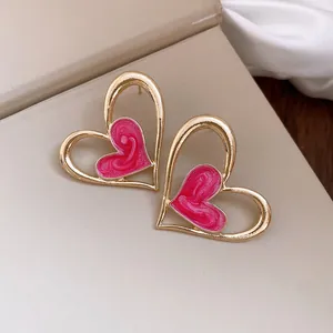Primer plano de pendientes de corazón dorados con esmalte rosa sobre fondo beige