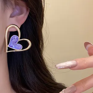 Detalle de pendientes de botón de corazón vintage en oro con esmalte morado y diseño elegante