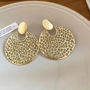 Detail von goldfarbenen runden hohlen Tropfenohrringen mit strukturiertem Muster.
