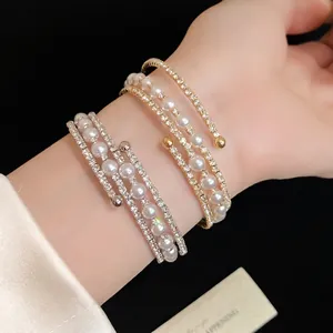 Elegant multi-layer open bracelet with pearls and rhinestones worn on a model's wrist.