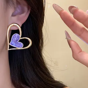 Primer plano de pendientes de corazón dorado con esmalte morado puestos en la oreja.
