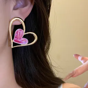 Primer plano de elegantes pendientes de corazón de oro con detalle de esmalte rosa.
