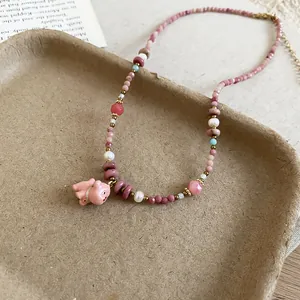 Detail of a pink beaded necklace with a cute ceramic pendant on a textured display tray.