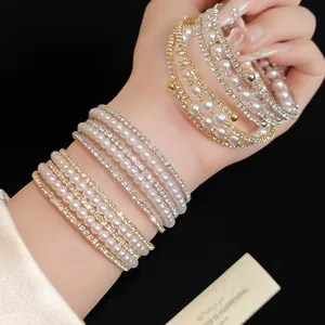 Close-up of elegant multi-layer bracelets featuring pearls and rhinestones on a wrist.