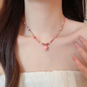 Close-up of pink ceramic puppy pendant and pearl beaded necklace worn on neck