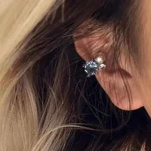 Detailed macro view of an elegant sparkling blue zircon and pearl ear cuff worn on the model's ear.