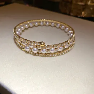 Elegant three-layer gold-plated open bracelet featuring white pearls and sparkling rhinestones