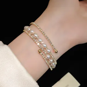 Detailed view of multi-layer gold bracelet with pearls and rhinestones on wrist.
