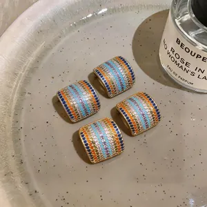Primer plano de cuatro pendientes cuadrados con circonitas de colores sobre un plato.