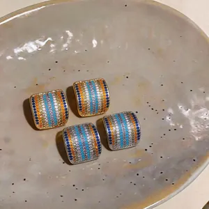 Primer plano de pendientes cuadrados con circonitas de colores en plato de cerámica