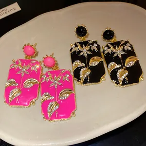 Close-up of vintage enamel floral earrings in pink and black with sparkling rhinestones.