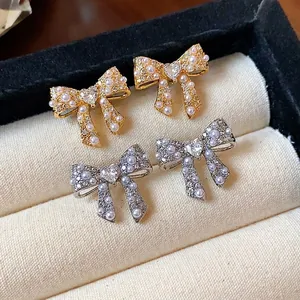 Elegant bowknot pearl stud earrings with heart-shaped crystal in gold and silver finish.