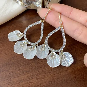 Close-up of elegant gold-tone teardrop earrings with sparkling rhinestones and white petals.