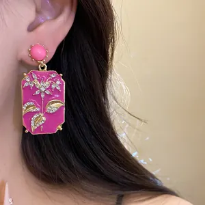 Close-up of pink enamel rectangular earrings with gold floral design and rhinestones
