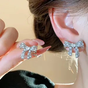 Detail view of silver bow earrings with pearls worn and held, showing delicate heart center.