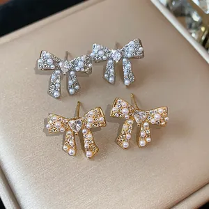Close-up detail of elegant bowknot earrings with pearls and heart zircon on satin.