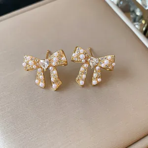 Close-up of 18k gold plated bow stud earrings with delicate pearls and heart crystal.