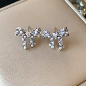 Close-up detail of 18k gold plated bow-knot pearl earrings with heart-shaped crystal