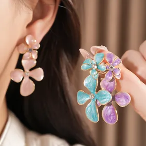 Close-up of colorful enamel flower earrings with rhinestones on a model's hand and ear